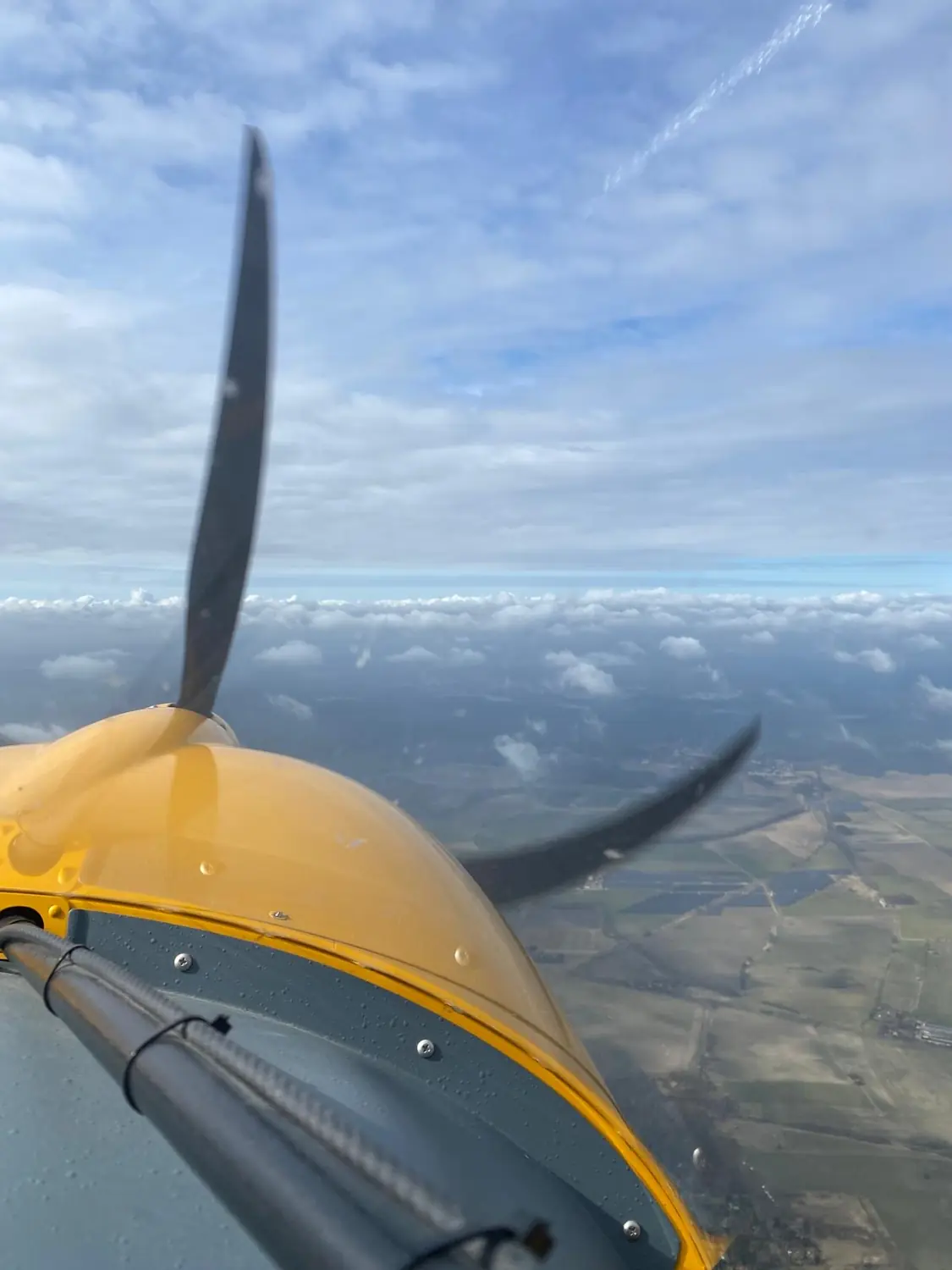 Blick über die gelbe Flugzeugnase und den Propeller auf Wolken und Landschaft